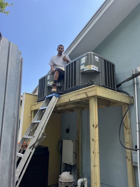 Gracie AC owner Jesus Park sitting on a wooden platform he built, next to two newly installed AC condensers